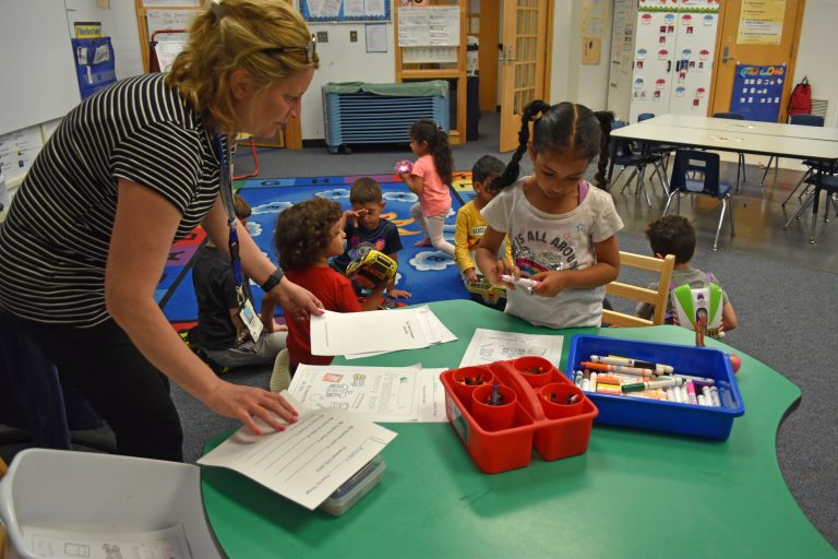 A teacher helps a student learn to write her name.